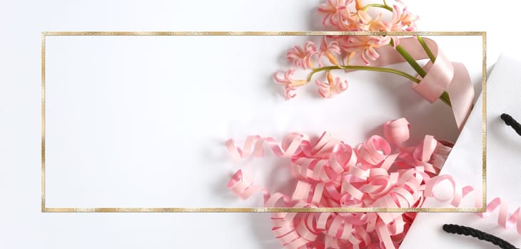Pink spring flowers, pink gift streamer in white gift bag on white background. Beautiful spring card for Birthday, Woman, Valentines, Mothers Day in pastel colours. Horizontal flat lay. Copy space