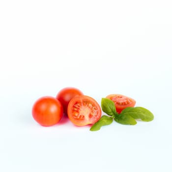 Red cherry tomatoes with green basil on a white background. High quality photo