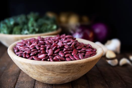Wooden bowl full of dried red beans with kale, garlic and other ingredinets in the background