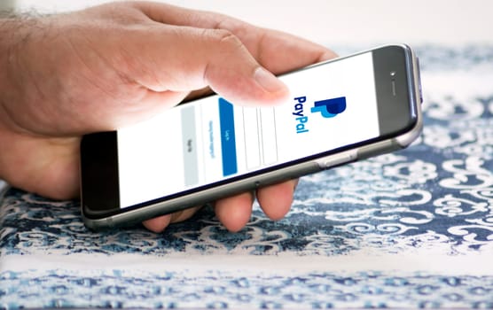 Rome, Italy, february 16th 2021: Hand holding a smart phone with Paypal app login page on screen. Money transfer and shopping online application