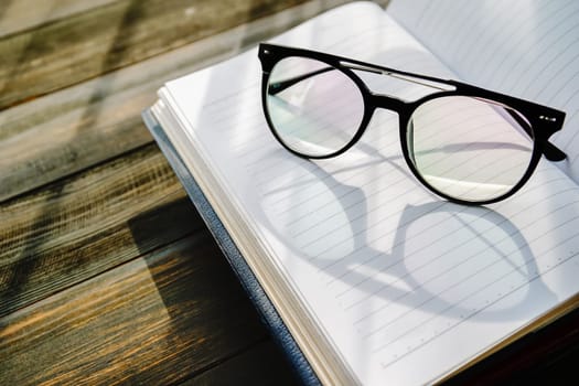Reading glasses put on open book over wooden table