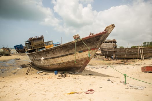 An old fishing boat is being repaired in the harbor by several workers.