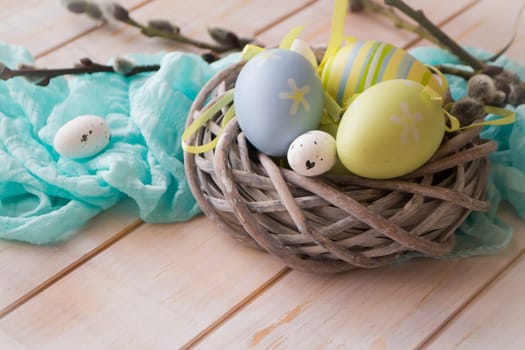 Easter background with colorful eggs in nest on a white shabby wooden background.