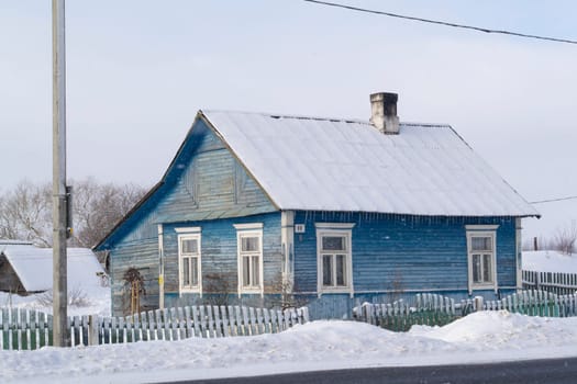 Old wooden blue house in village. Farmhouse in Belarus. View of rustic ethnic house, rural landscape in winter