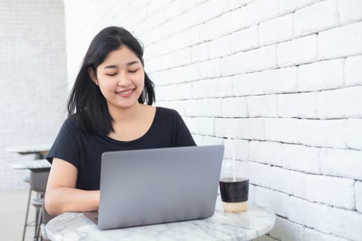 Young Asian woman freelance is working with laptop at coffee shop. Business woman typing, searching in modern cafe. Working online technology system concept.