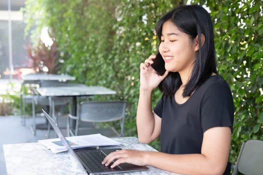 Young Asian woman freelance is working with laptop at coffee shop. Business woman typing, searching and checking document in modern cafe.  Working online technology system concept.