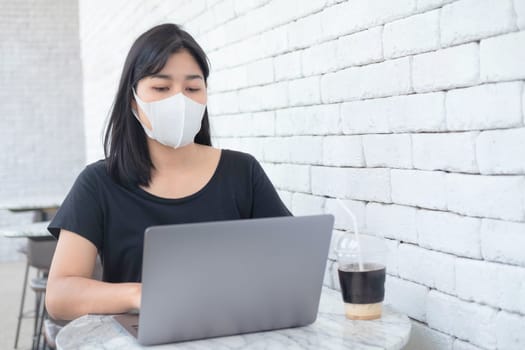 Young Asian woman freelance wearing medical masks working with laptop at coffee shop. New normal and social distance working. .