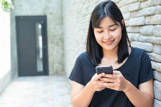 Smiling young woman reading text message or social media on cell telephone. Asian female chatting during wait her friends. Relaxing time, Chill out life.