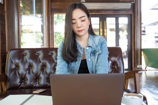 Young Asian woman freelance is working with laptop at coffee shop. Business woman using laptop computer and drinking coffee in modern cafe. Working online technology system concept.