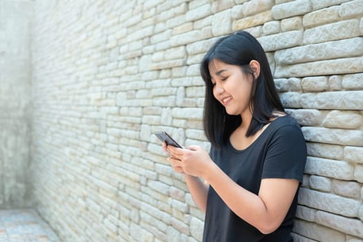 Smiling young woman reading text message or social media on cell telephone. Asian female chatting during wait her friends. Relaxing time, Chill out life.