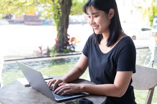 Young Asian woman freelance is working with laptop at coffee shop. Business woman typing, searching and checking document in modern cafe. Working online technology system concept.