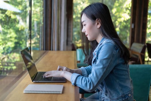 Young Asian woman freelance is working with laptop at coffee shop. Business woman typing, searching and checking document in modern cafe.  Working online technology system concept.