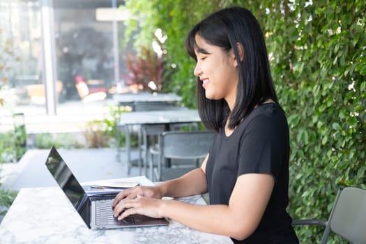 Young Asian woman freelance is working with laptop at coffee shop. Business woman typing, searching and checking document in modern cafe.  Working online technology system concept.