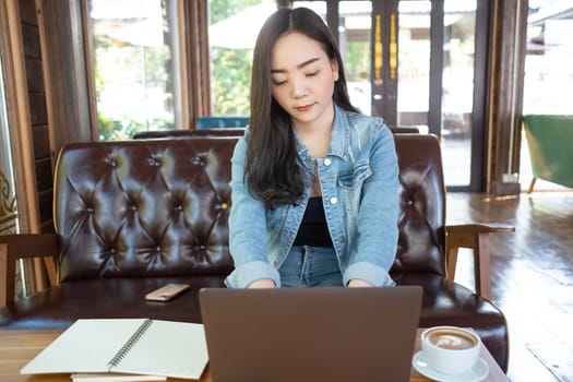 Young Asian woman freelance is working with laptop at coffee shop. Business woman using laptop computer and drinking coffee in modern cafe. Working online technology system concept.