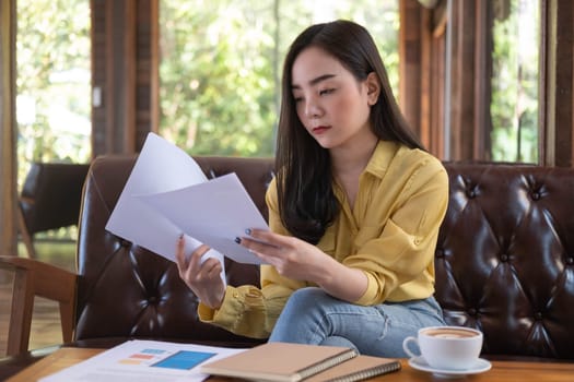 Young Asian businesswoman sitting in cafe and reading documents. Female working with financial documentation and financial reports before meeting.