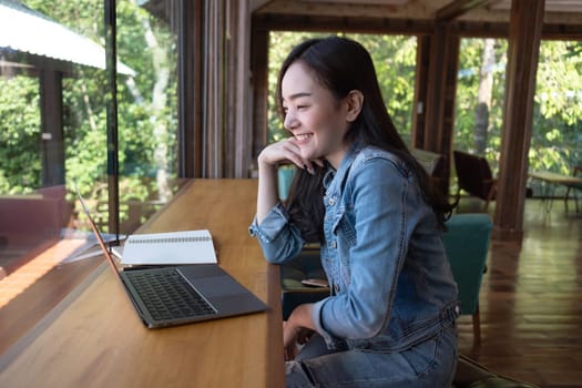 Young Asian woman video calling with her friend on laptop at coffee shop. Working online technology system concept.