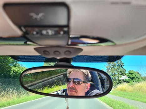 Reflection of senior mans eyes in rearview mirror of car with wet windshield