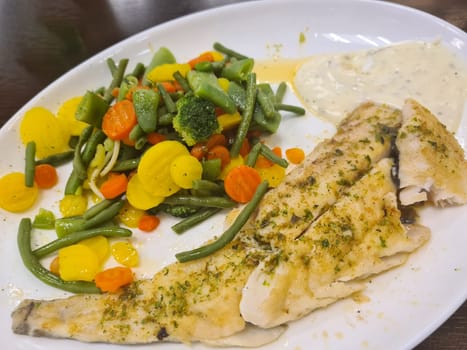 To portions of fresh grilled pollock or coalfish served with colorful salad and slices of lemon, close up high angle view