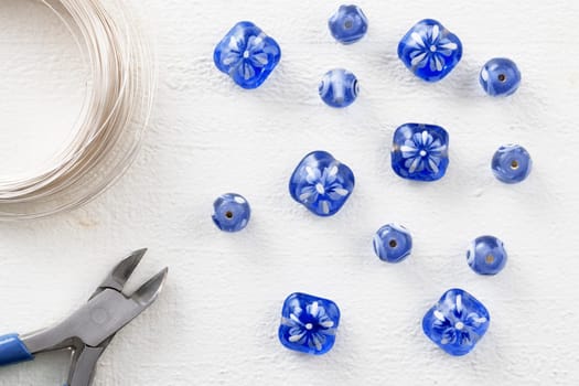 Blue and white glass beads with wier cutters, and beading wire, on white painted wooden surface, top down view