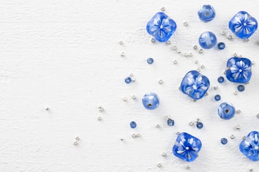 Blue and white glass beads with silver sead beads, on white painted wooden surface, top down view