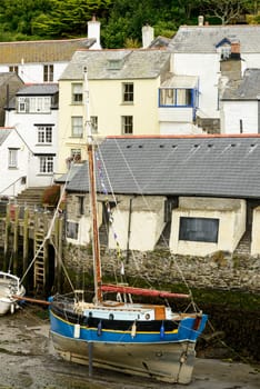 cityscape of the touristic village on southern coast of Cornwall with low tide in the river harbour and old sailboat aground in foreground.