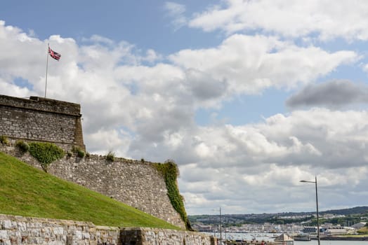 view of the huge wall that encloses the area of the castle and cityscape of  historic sea town of Devon under a bright cloudy sky.