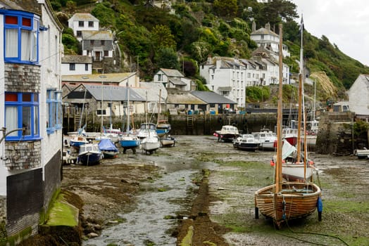 cityscape of the touristic village on southern coast of Cornwall with low tide in the river harbour and boats aground .