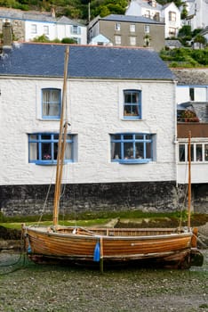 cityscape of the touristic village on southern coast of Cornwall with low tide in the river harbour and old wooden  boat aground.