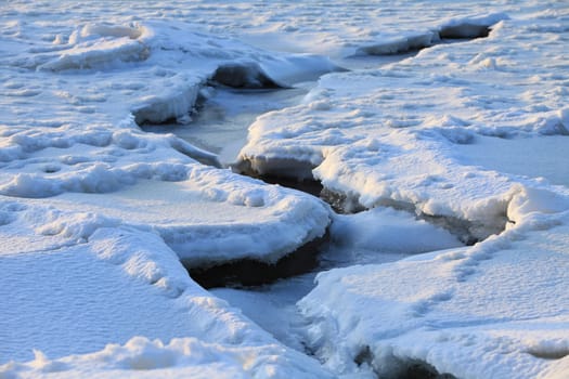 deep winding crack in the ice of a frozen river covered with snow winter landscape