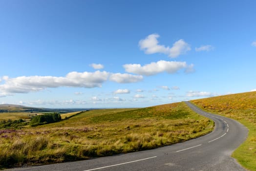 landscape with an empty road bending uphill in  Dartmoor countryside.
