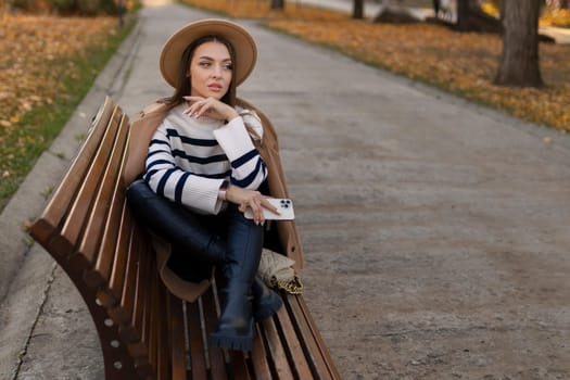beautiful smiling woman in stylish outfit sitting at the table in a hat and sweater, romantic happy mood, waiting for a boyfriend on a date in a cafe, spring-summer fashion trend, drinking coffee.