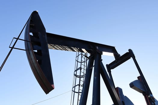 Silhouette of the oil pumpjack head against a blue sky.