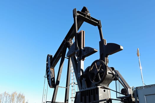 Silhouette of the oil pumpjack head against a blue sky.