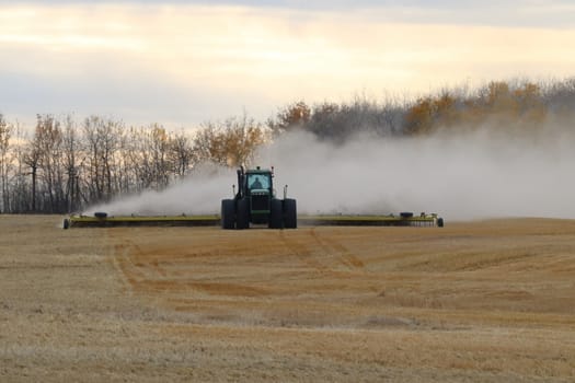 BONNYVILLE, ALBERTA, CANADA - SEPTEMBER 10, 2020: A local farmer in John Deere tractor works infront of a cloud of dust as he levels a harvested field.