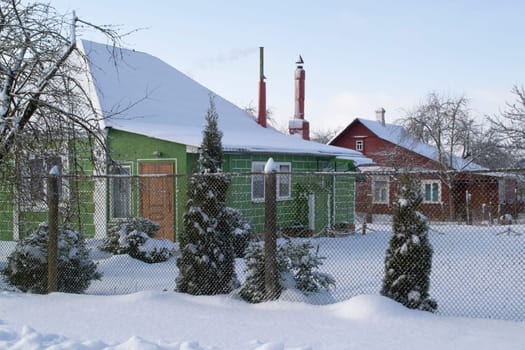 The snow covered yard of the wooden house in belarussian village. Old country house in winter