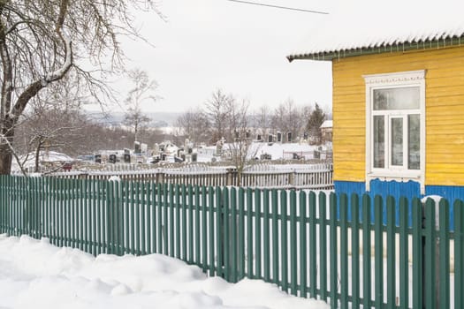 An old cemetery with tombstones and large wooden crosses in belarussian village with old wooden rustic houses. Western Belarus, Slonim