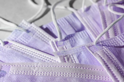 Many disposable 3-ply purple face masks in a pile. Elastic ear loop style masks often associated with surgical or medical use. Coronavirus relevance.