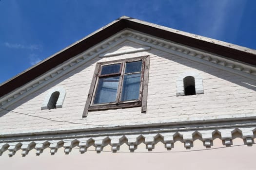 Attic window vent on old white brick, old house in Belarus, with blue sky background