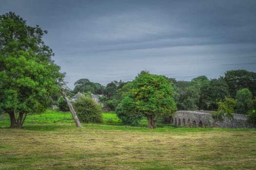 Old, 12th century stone arch Bective bridge over Boyne River in Bective village. Green fields or pastures and trees, Count Meath, Ireland