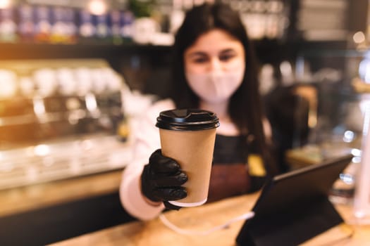 Barista in protective face mask and black gloves gives cup of coffee in cafe. High quality photo