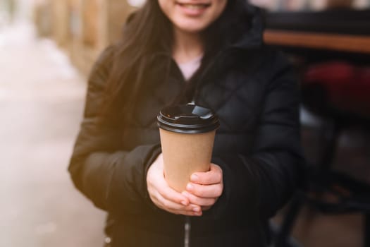 Smiling girl holds a paper cup of coffee in hand near cafe. High quality photo