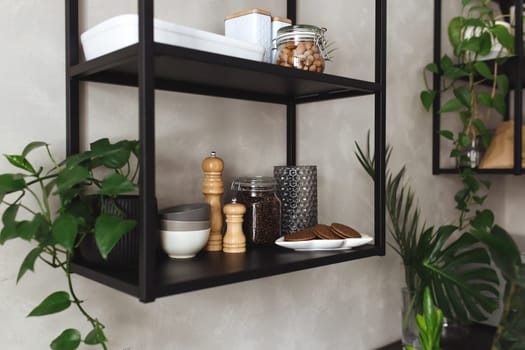 Black metal shelves in the kitchen on a gray concrete wall in a loft style. Green flowerpots. High quality photo