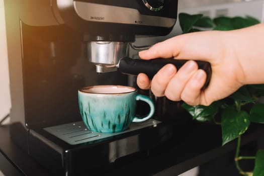 Hand holding portafilter, green cup of coffee at the coffee maker machine, coffee time. Blurred background. High quality photo