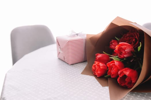 A bouquet of red tulips on the table and pink gift box. Concept for a greeting card. High quality photo