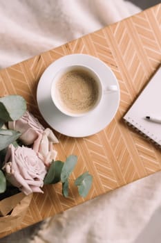 Romantic morning. Wooden coffee table with flowers on bed flat lay, coffee cup, flowers, note pad, pen. Lilac roses with eucalyptus and anemones. High quality photo