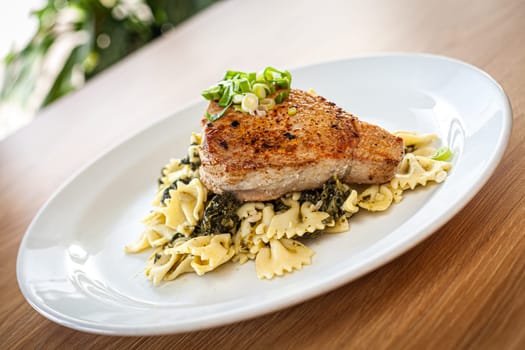 Cooked food on a white plate - tuna served on spinach pasta.