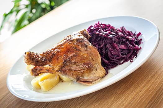 Cooked food on a white plate - roasted duck leg, red cabbage, potato dumplings.