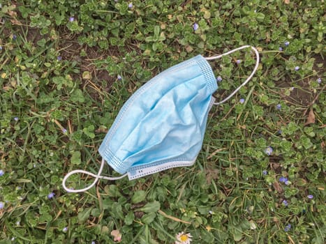 Surgical face mask abandoned on the ground into grass. Coronavirus covid-19 pandemic.