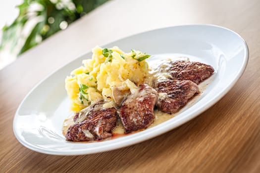 Cooked food on a white plate - pork tenderloin with bra, pine nuts and spring onions.