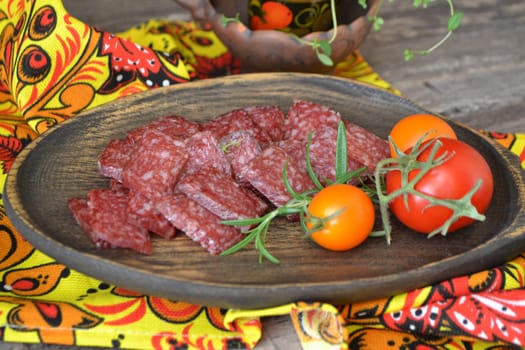 Salami sausages sliced on wooden rustic plate with tomatoes and rosemary